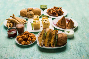 Indian Tea time snacks  in group includes Veg Samosa, Kachori/kachaudi, aloo bonda, khaman dhokla, bread, onion,chilli and moong pakora/pakoda/bhaji/bhajji/Bhajiya/bajji with sauces, selective focus