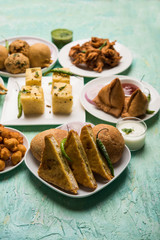 Indian Tea time snacks  in group includes Veg Samosa, Kachori/kachaudi, aloo bonda, khaman dhokla, bread, onion,chilli and moong pakora/pakoda/bhaji/bhajji/Bhajiya/bajji with sauces, selective focus