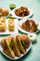 Indian Tea time snacks  in group includes Veg Samosa, Kachori/kachaudi, aloo bonda, khaman dhokla, bread, onion,chilli and moong pakora/pakoda/bhaji/bhajji/Bhajiya/bajji with sauces, selective focus