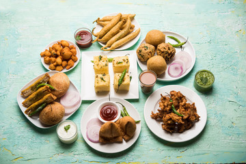Indian Tea time snacks  in group includes Veg Samosa, Kachori/kachaudi, aloo bonda, khaman dhokla, bread, onion,chilli and moong pakora/pakoda/bhaji/bhajji/Bhajiya/bajji with sauces, selective focus