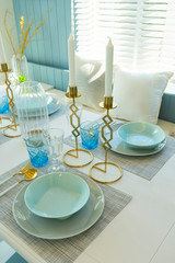 Pale blue plate setting on table with gold candle holder in home dining room interior. 