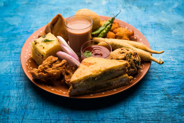 Indian Tea time snacks  in group includes Veg Samosa, Kachori/kachaudi, aloo bonda, khaman dhokla, bread, onion,chilli and moong pakora/pakoda/bhaji/bhajji/Bhajiya/bajji with sauces, selective focus