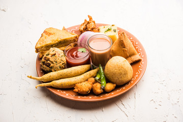 Indian Tea time snacks  in group includes Veg Samosa, Kachori/kachaudi, aloo bonda, khaman dhokla, bread, onion,chilli and moong pakora/pakoda/bhaji/bhajji/Bhajiya/bajji with sauces, selective focus