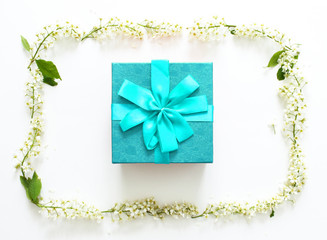Blue gift box with blue ribbon and round frame made of white flowers on white background. Christmas, Valentine's day or birthday concept. Place for text.Top view, flat lay. Flowers composition. 