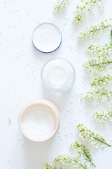 Set of bowls with moisturizer cream. Various facial cosmetic products. Top view of composition with cosmetic products and flowers on white background.Place for your text or logo.Beauty background.