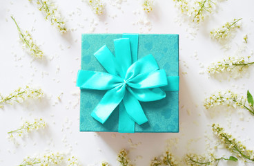Surprise blue gift box. Blue gift box with blue ribbon and round frame made of white flowers on white background. Christmas, Valentine's day or birthday concept. Place for text.Top view, flat lay.