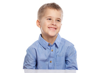 Cute boy of school age sits at the table and laughs. Isolated on a white background.