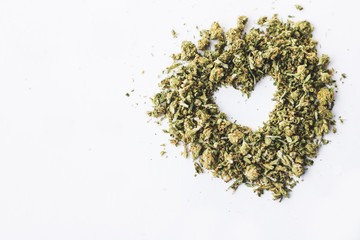 Heart made of crushed up marijuana herb isolated on white background
