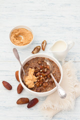 Delicious oatmeal in a white bowl, dates fruits, cocoa and vegan milk. healthy breakfast on light blue background. top view