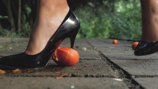 foot girl close up in black patent-leather shoes crushed a mandarin on a concrete tile in the street and pierces with a heel. foot fetish. 4k. 4k video
