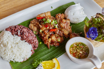 Pork fried with oyster sauce served with rice berry, white rice in banana leaf above white disk. Top view. Close up and selective focused.