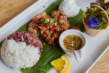 Pork fried with oyster sauce served with rice berry, white rice in banana leaf above white disk. Top view. Close up and selective focused.