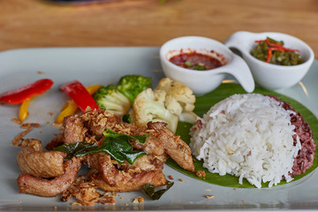Pork fried with oyster sauce served with rice berry, white rice in banana leaf above white disk. Top view. Close up and selective focused.