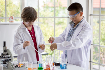 Group of Pupils boy in white gown doing a chemical experiment in laboratory at school . kids in science lab study using pipette dropping liquid to test tube. asian ,caucasian, chemistry class