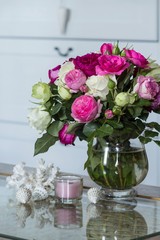 Female Interior - bouquet of fragrant pink and white English roses, shells and pink candle on the glass table
