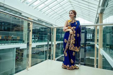Young elegant indian business woman in a stylish blue sari arms crossed in a modern office with...
