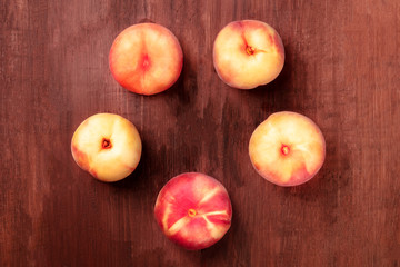 Vibrant organic flat saturn peaches, shot from the top on a dark rustic wooden background forming a circle for copy space