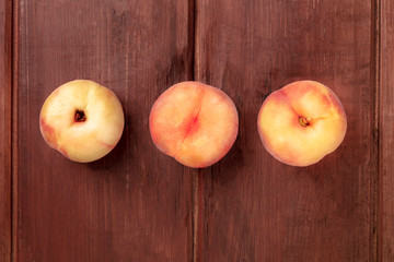 An overhead photo of vibrant organic flat saturn peaches on a dark rustic wooden background with copy space