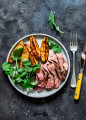 Beef steak and baked young potatoes - delicious lunch on a dark background, top view