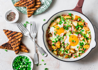 Potatoes, ham, eggs breakfast hash in a frying pan on a light background, top view. Delicious,...