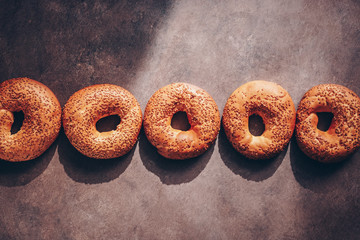 Homemade bagel with sesame in a row on a dark rustic background with hard shadows and light. Top...