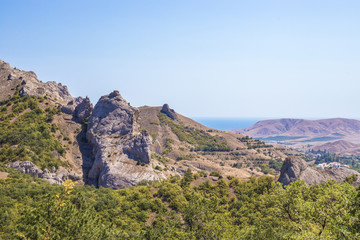 Crimean mountain peaks among green bushes and the sea against the blue sky