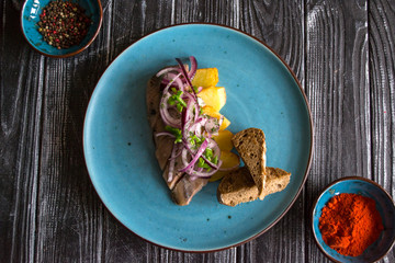 Fried potatoes and herring fish with onion on a wooden table.