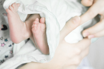Soft newborn baby feet on mother's hands in white clothes