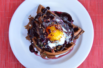 Waffles with sunny side up egg topped with blueberry sauce and nuts crumble