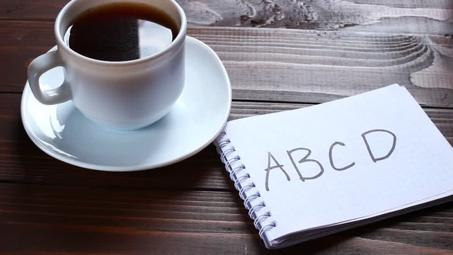 ABCD inscription and word in a notebook near a cup of coffee