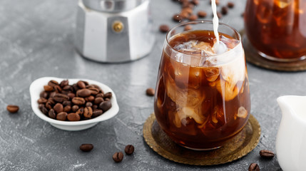 Summer drink iced coffee or caffe latte in a glass with milk and coffee beans.