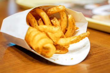 Spiral french fries in white box and on wooden table and blurry background.