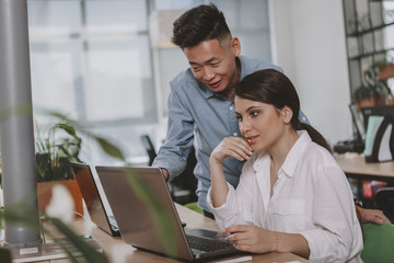 Young Asian businessman and his female colleague using laptop at work together. Attractive businesswoman working with her colleague, browsing online on her computer, copy space