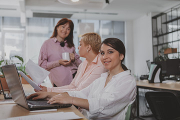 Group of successful businesswomen working at the office together. Lovely young businesswoman smiling to the camera, her female colleagues talking on the background. Startup, equality concept