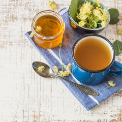 A mug of hot tea, fresh linden flowers and a glass jar with honey on a blue napkin on a wooden table. Prevention and treatment of flu and colds. Selective focus.