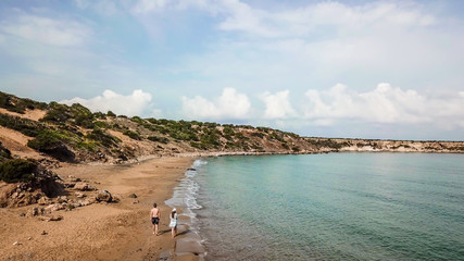 A couple walking along Lara Beach in Cyprus. Hidden gem, not spoiled by tourists. Solitude and calm feelings, waves gently spreading on the beach. turquoise color of the water. Turtle hatching beach