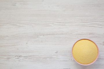 Dry semolina durum flour in a pink bowl over white wooden background, overhead view. Top view, from above, flat lay. Copy space.
