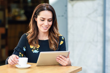 Middle-aged woman using tablet on coffee break in urban cafe bar.