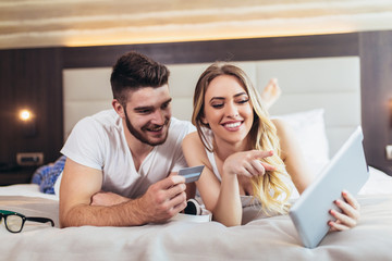 Obraz na płótnie Canvas Pretty couple with credit card and digital tablet lying in bed and doing online shopping