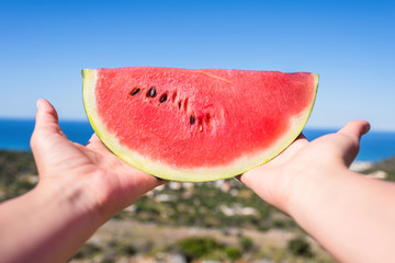 Ripe piece of watermelon in female hands on the background of the sea on a hot summer day. Concept