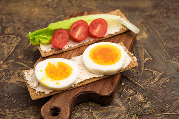 crispbread with egg, cherry tomatoes and a fresh leaf of lettuce on a wooden cutting board. Snacks