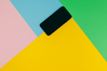 A black phone is laying on a flat surface of green, blue, pink, and yellow