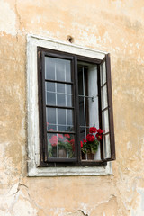 Fototapeta na wymiar Half-open window with flowers of a old building