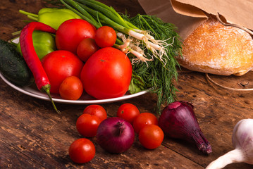 Fresh vegetables, tomatoes, cherry tomatoes, green peppers, chilli peppers, onions, cucumbers, garlic and herbs and ciabatta bread in a paper bag on a rustic wooden table - Italian rural style
