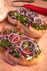 Traditional Italian veggie bruschetta sandwich with ciabatta toasts with sliced tomatoes, chili pepper, spring  and red onions and herbs and olive oil close-up
