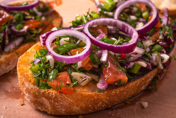 Traditional Italian veggie bruschetta sandwich with ciabatta toasts with sliced tomatoes, chili pepper, spring  and red onions and herbs and olive oil close-up