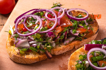 Traditional Italian veggie bruschetta sandwich with ciabatta toasts with sliced tomatoes, chili pepper, spring  and red onions and herbs and olive oil close-up