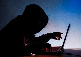 An anonymous hooded person sits in front of a computer. Concept computer crime.