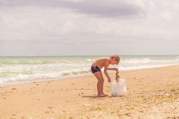 little boy picking up trash by the sea in summer