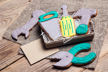 A set of gingerbread in the form of hand tools  on a wooden table with blank card for text. Tasty creative cookies for men's holidays.